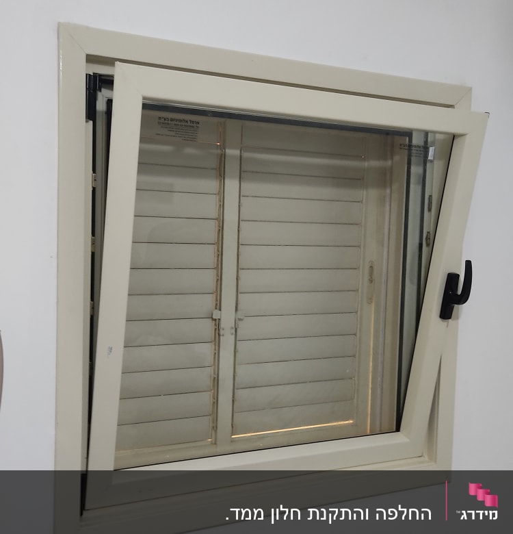 חלון אלומיניום עם ידית שחורה על קיר לבן